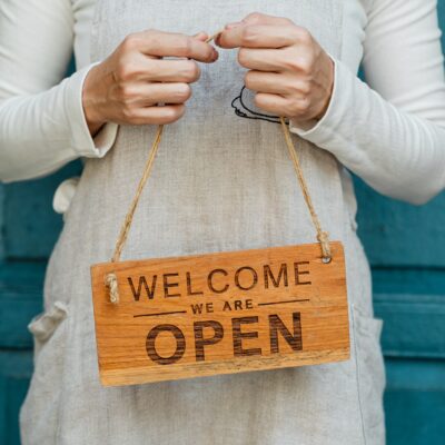 small business owner holds a sign that says Welcome