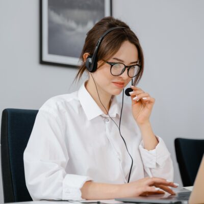 A woman sits at her computer while wearing a headset